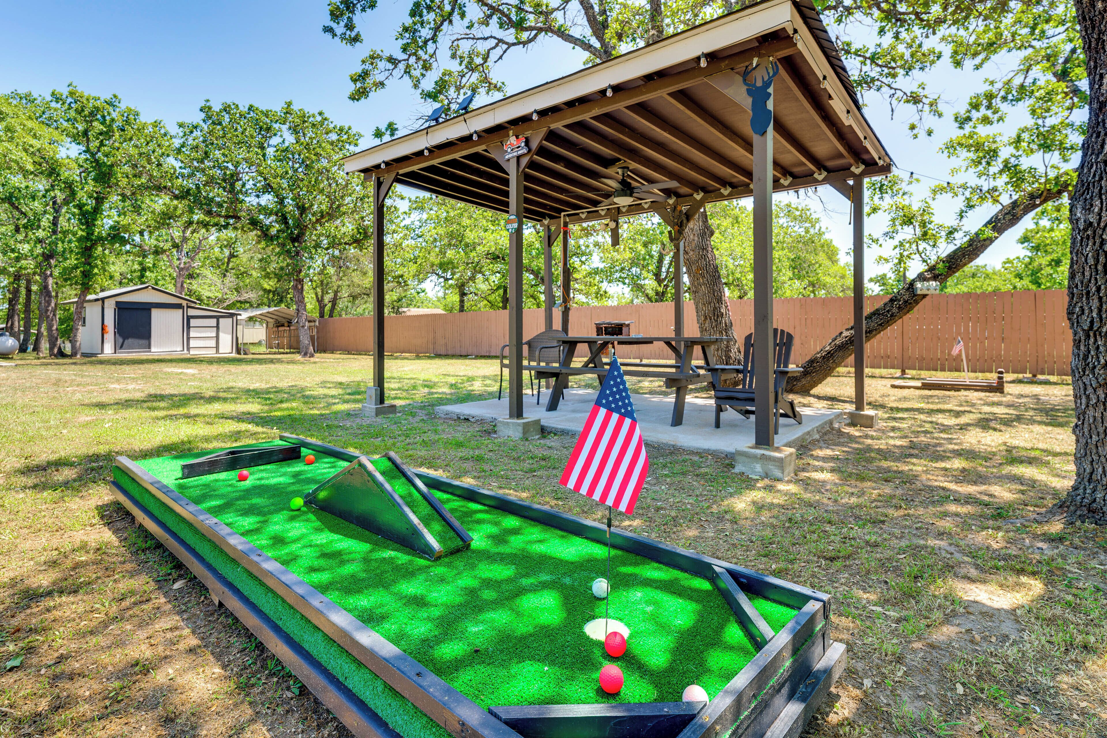 Un campo de mini golf con una estructura de madera, una bandera y una mesa de picnic.