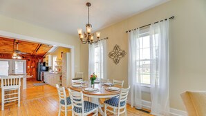 A dining area with a wooden table, white chairs, and a chandelier. - Home w/ Fire Pit < 1 Mi to Willis Wharf Boat Ramp! (Exmore)