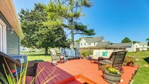 A deck with wicker furniture and a red floor, surrounded by a wooden fence and a large tree. - Home w/ Fire Pit < 1 Mi to Willis Wharf Boat Ramp! (Exmore)
