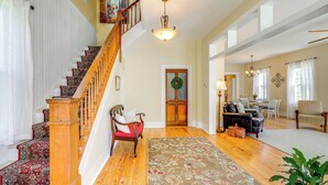 A spacious living room with hardwood floors, a large floral rug, a staircase with a wooden railing, a dining area with a table and chairs, and a cozy seating area with a sofa and armchairs. - Home w/ Fire Pit < 1 Mi to Willis Wharf Boat Ramp! (Exmore)