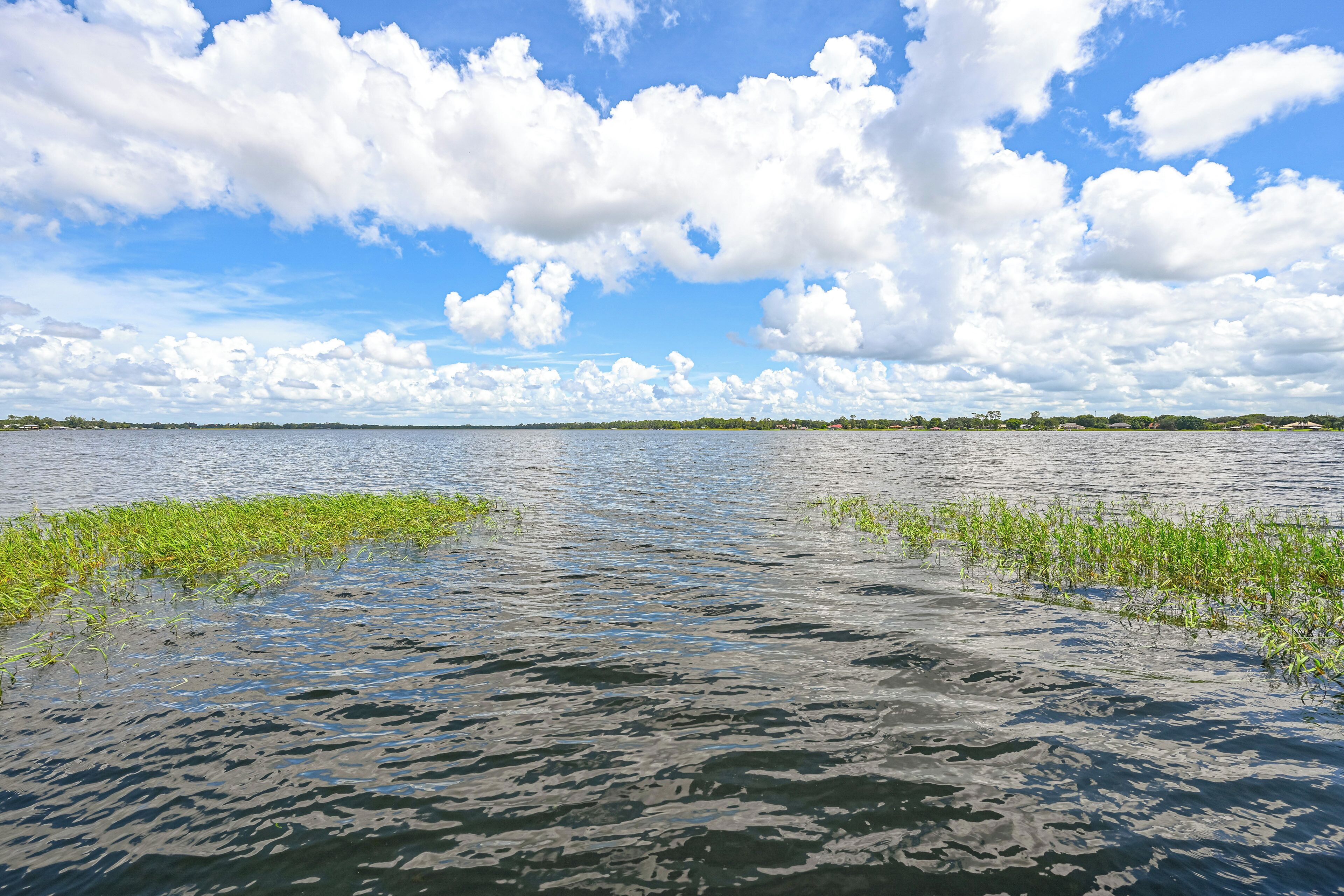 A calm lake with clear skies and scattered clouds.