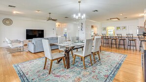 A spacious living area with a large TV, grey sofas, a dining table with chairs, and a kitchen area with bar stools. - Waterfront Home w/ Boat Dock in Lake Placid! (Lake Placid)