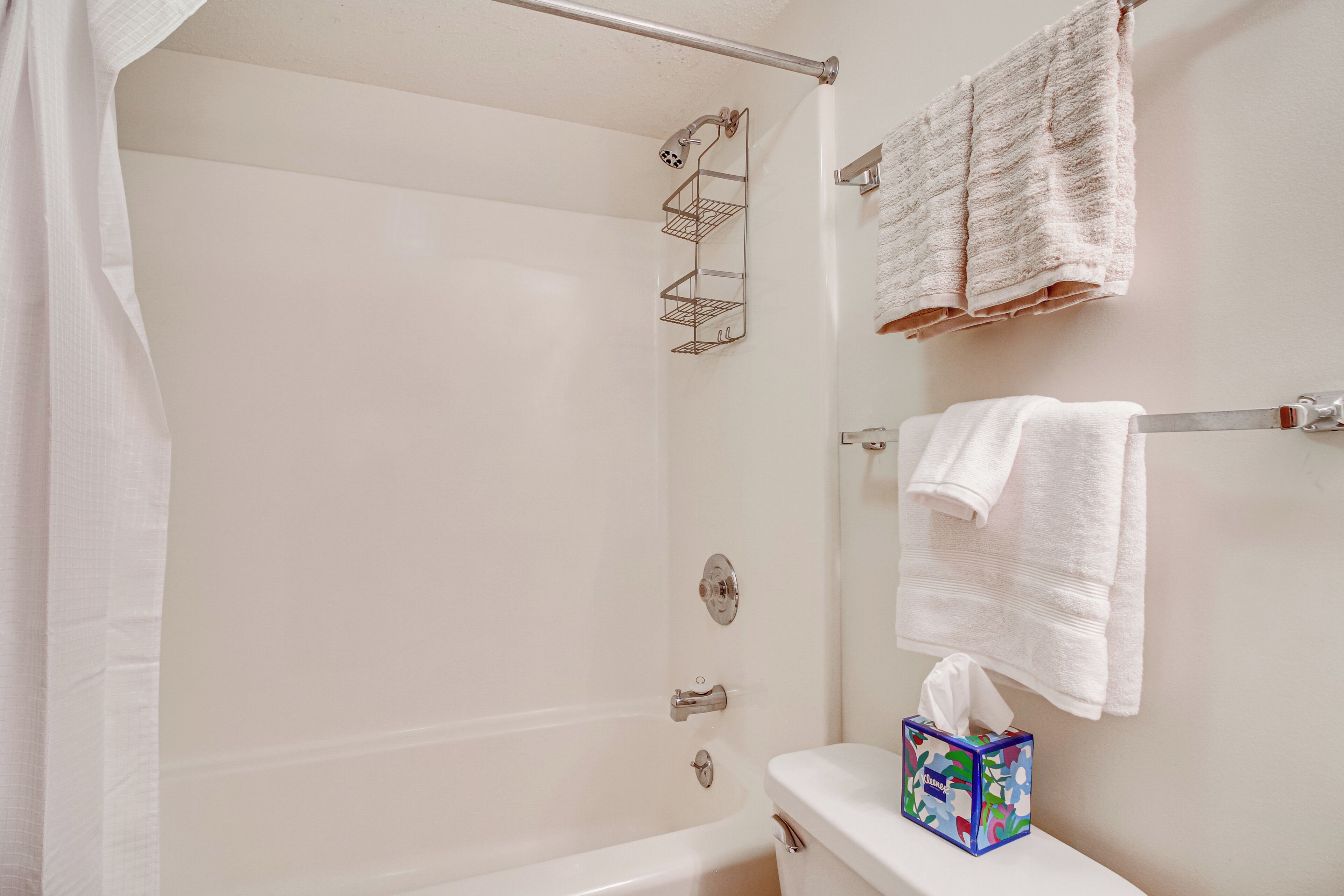 A bathroom with a bathtub, a toilet, a towel rack with towels, and a tissue box on the toilet.