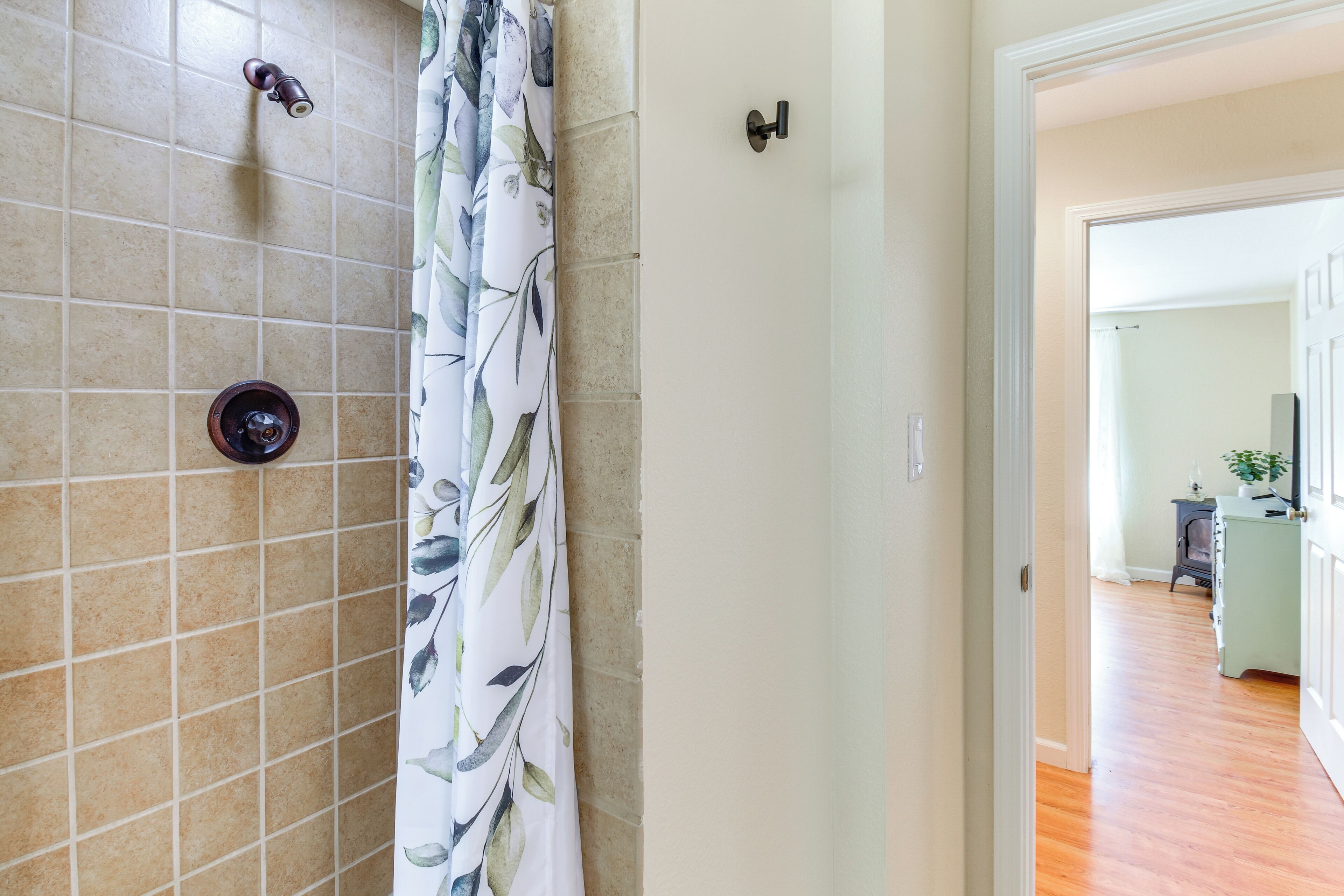 A bathroom with tiled walls, a shower curtain, and a door leading to a hallway with wooden flooring.