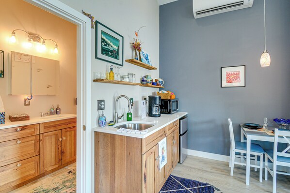 A modern kitchen with wooden cabinets, a built-in sink, and a dining area with a table and chairs. - Studio w/ Bay View: Beach Access! Octopus's Garden (Bremerton)