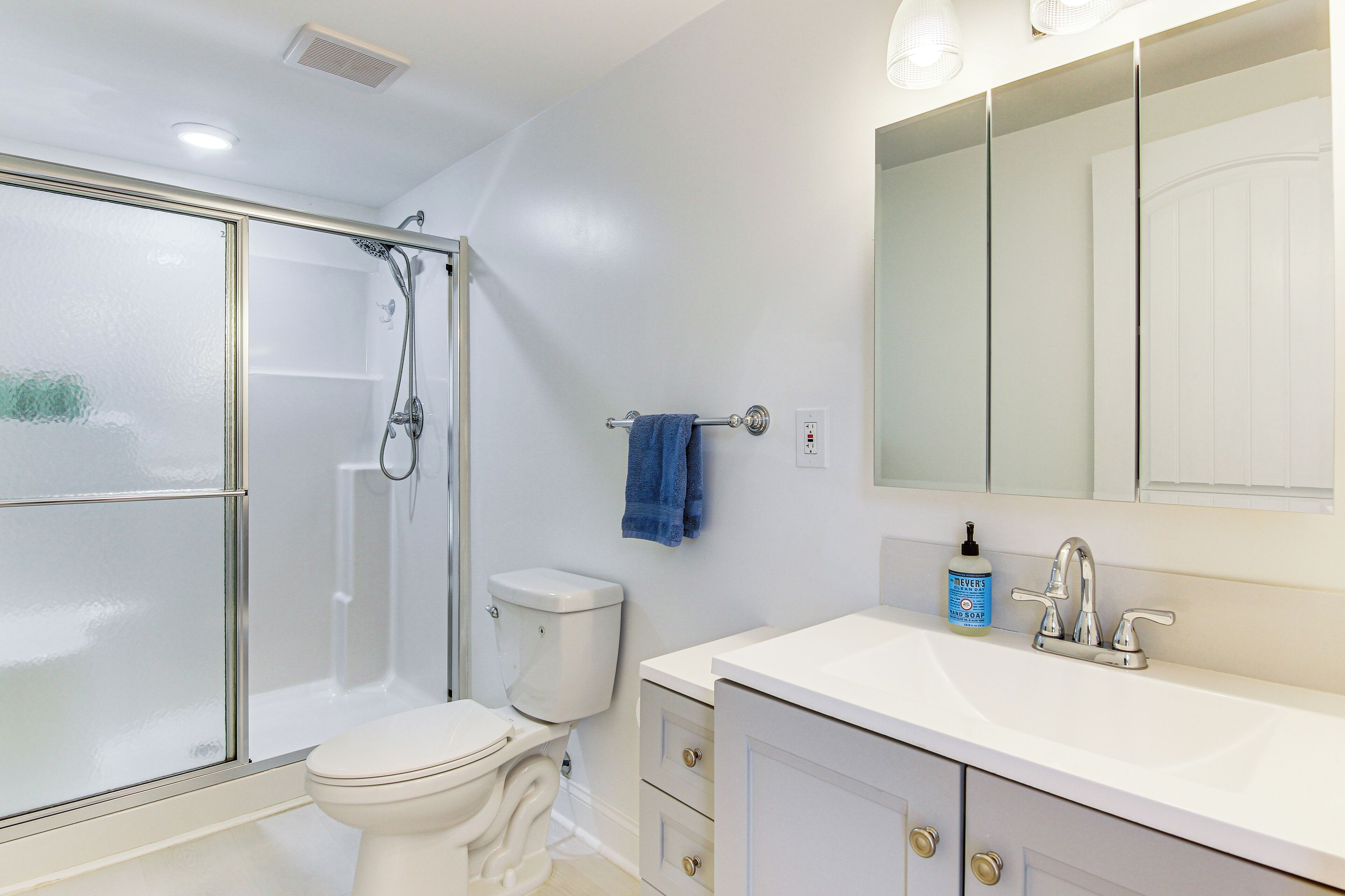 A bathroom with a glass-enclosed shower, a toilet, a sink with a mirror, and a blue towel hanging on a rack.