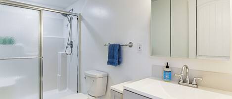 A bathroom with a glass-enclosed shower, a toilet, a sink with a mirror, and a blue towel hanging on a rack.