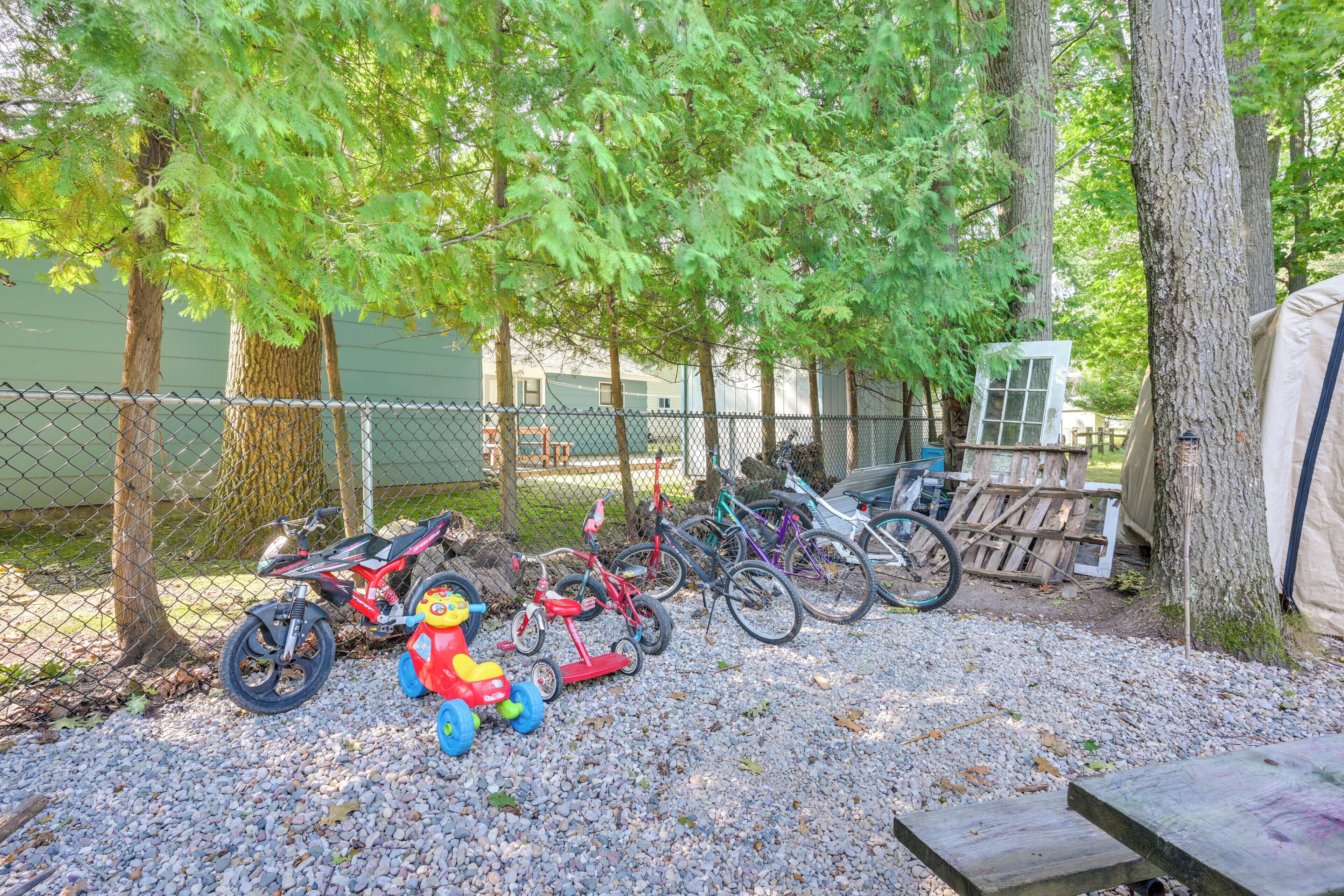 A gravel area with a chain-link fence, a red and yellow toy car, and several bicycles.