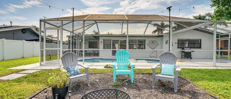 Un patio trasero con un porche techado, dos sillas Adirondack, un brasero y una piscina.