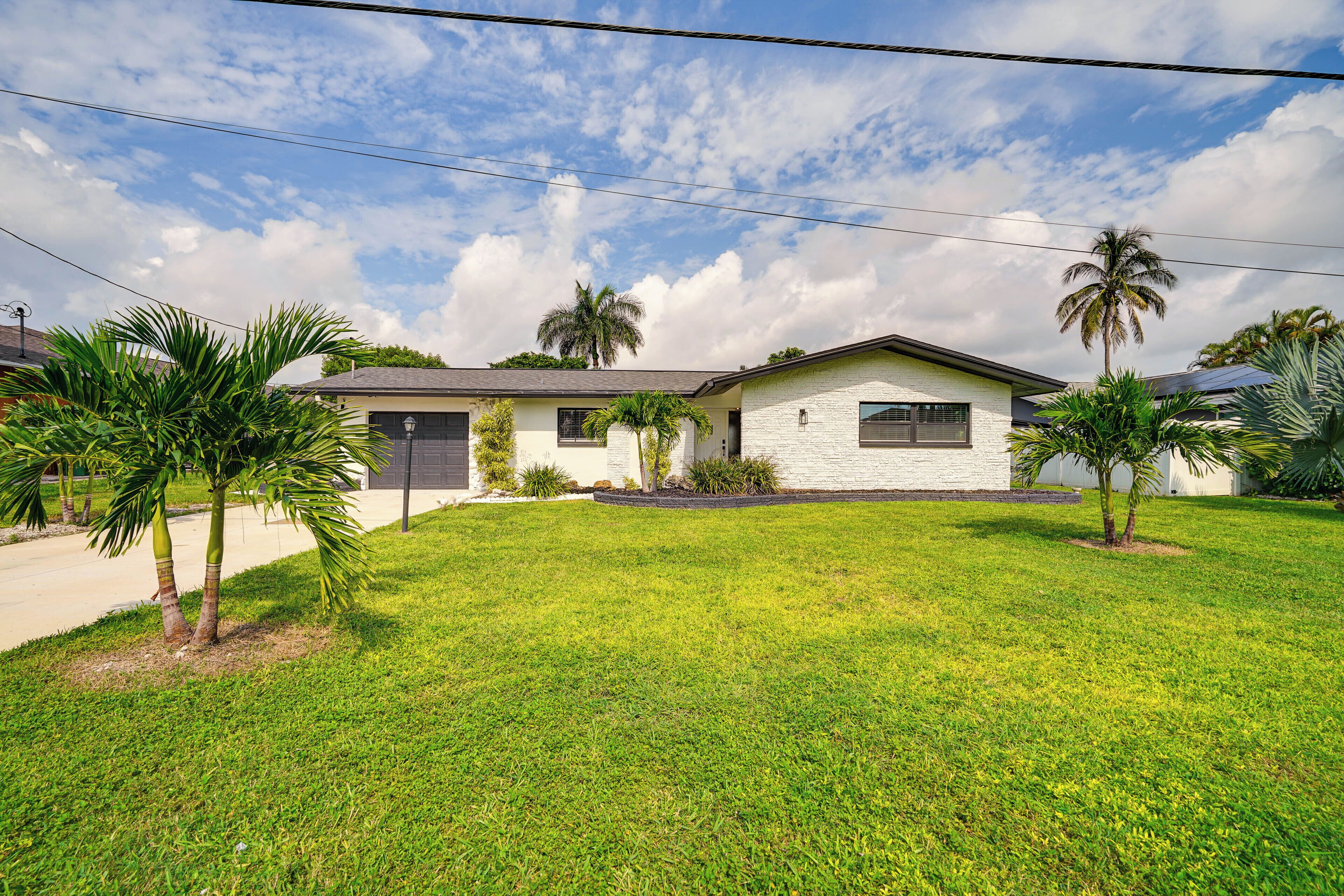 A two-story house with a well-maintained lawn and palm trees.