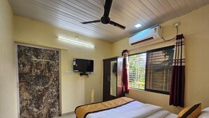 A bedroom with a bed, a ceiling fan, an air conditioner, a TV mounted on the wall, and a window with curtains. - Shanti Forest Resort (Karjat)