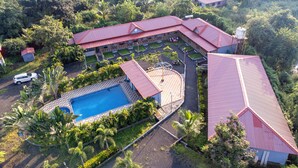 An aerial view of a resort with multiple buildings, a swimming pool, and lush greenery. - Shanti Forest Resort (Karjat)