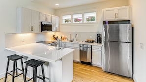 A modern kitchen with white cabinetry, stainless steel appliances, and a central island with bar stools. - 12 South Neighborhood: Home w/ Modern Flair! (Nashville)