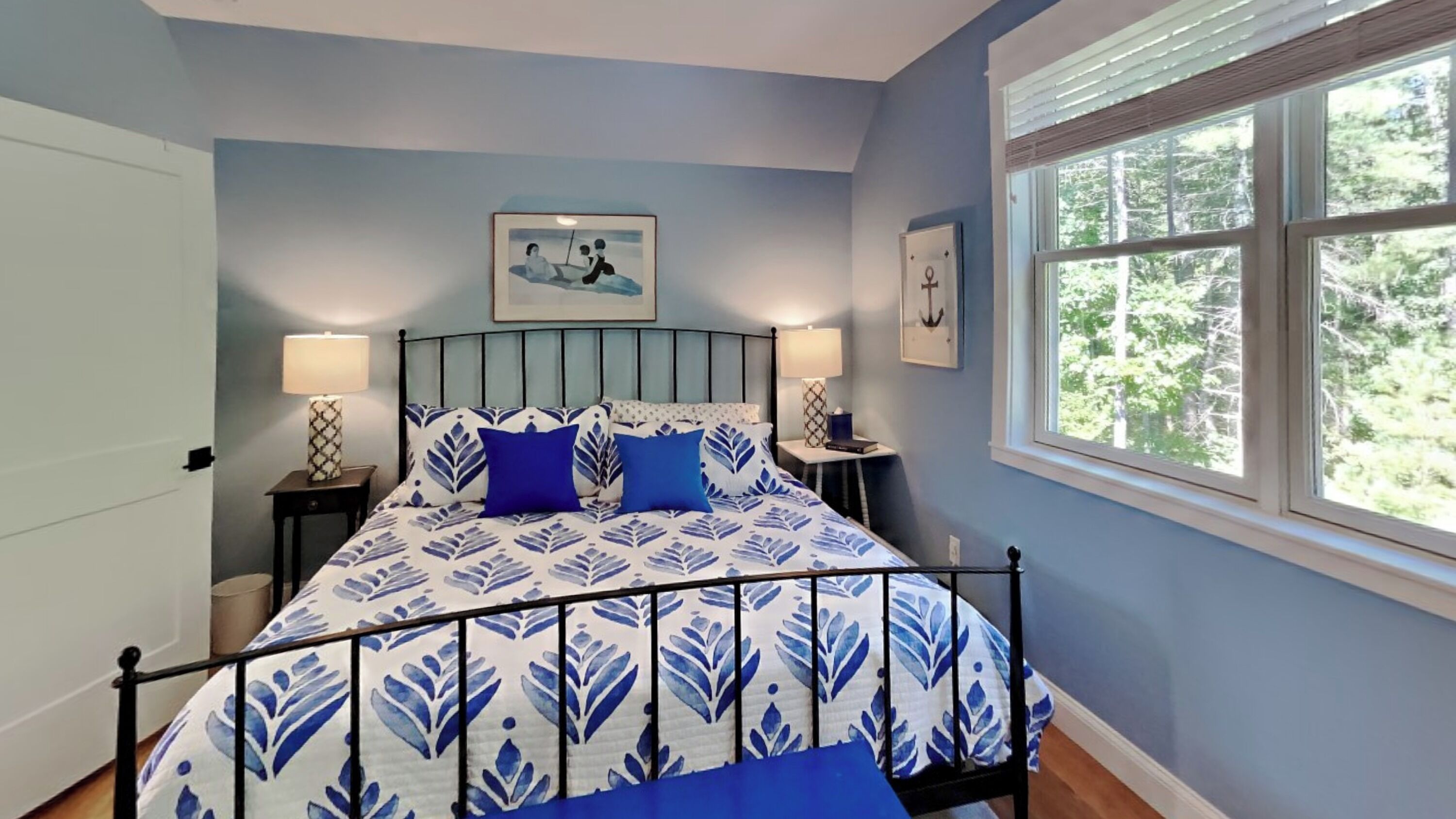 A bedroom with a bed, two bedside tables, a window, and a painting on the wall.