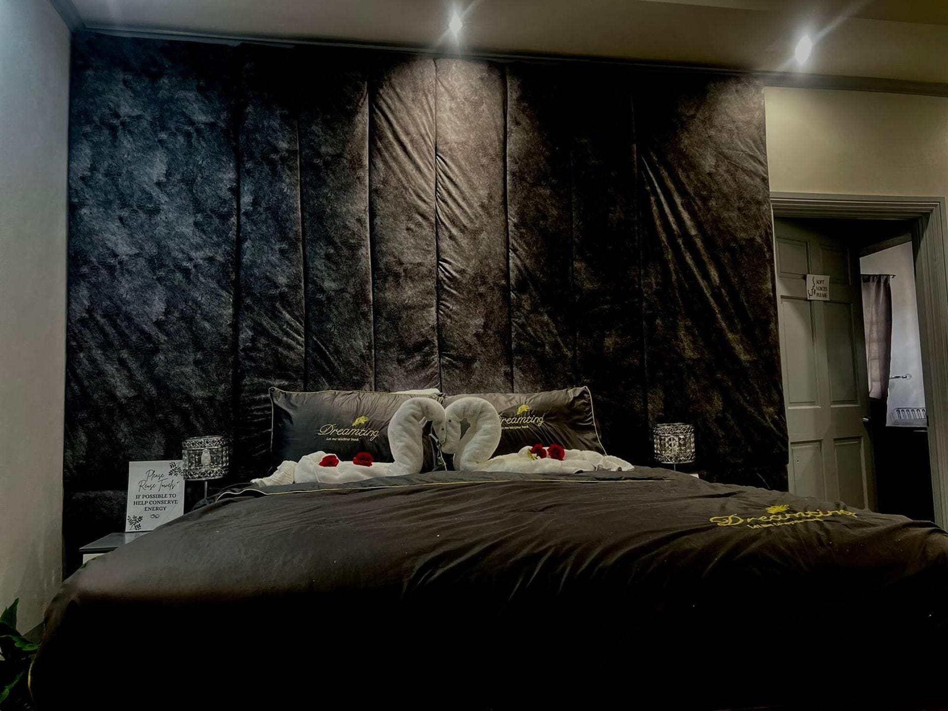 A bedroom with a dark, textured headboard, a bed with a black bedspread, and two heart-shaped pillows.