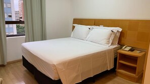 Una camera d'albergo con un letto, un comodino con il telefono e una finestra con tende.