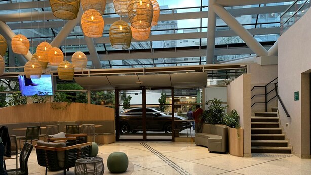 A modern lobby with a glass ceiling, wicker hanging lights, seating areas, and a staircase. - Get a Flat 604 - Jardim Paulista  (São Paulo)