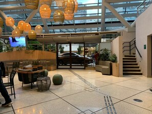 A modern lobby with a glass ceiling, wicker hanging lights, seating areas, and a staircase. - Get a Flat 604 - Jardim Paulista  (São Paulo)