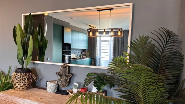 A modern kitchen with a large mirror, wooden cabinetry, and various plants. - Caparica Surf Retreat (Almada)