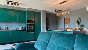 A modern kitchen with teal cabinetry, a built-in oven, and a dining area with a teal sofa. - Caparica Surf Retreat (Almada)