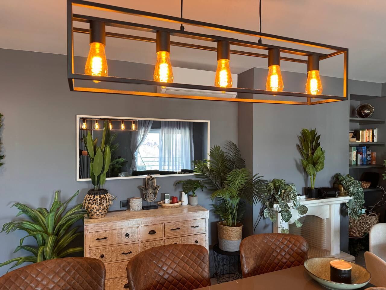 A dining area with a wooden cabinet, chairs, a table, and a hanging light fixture.