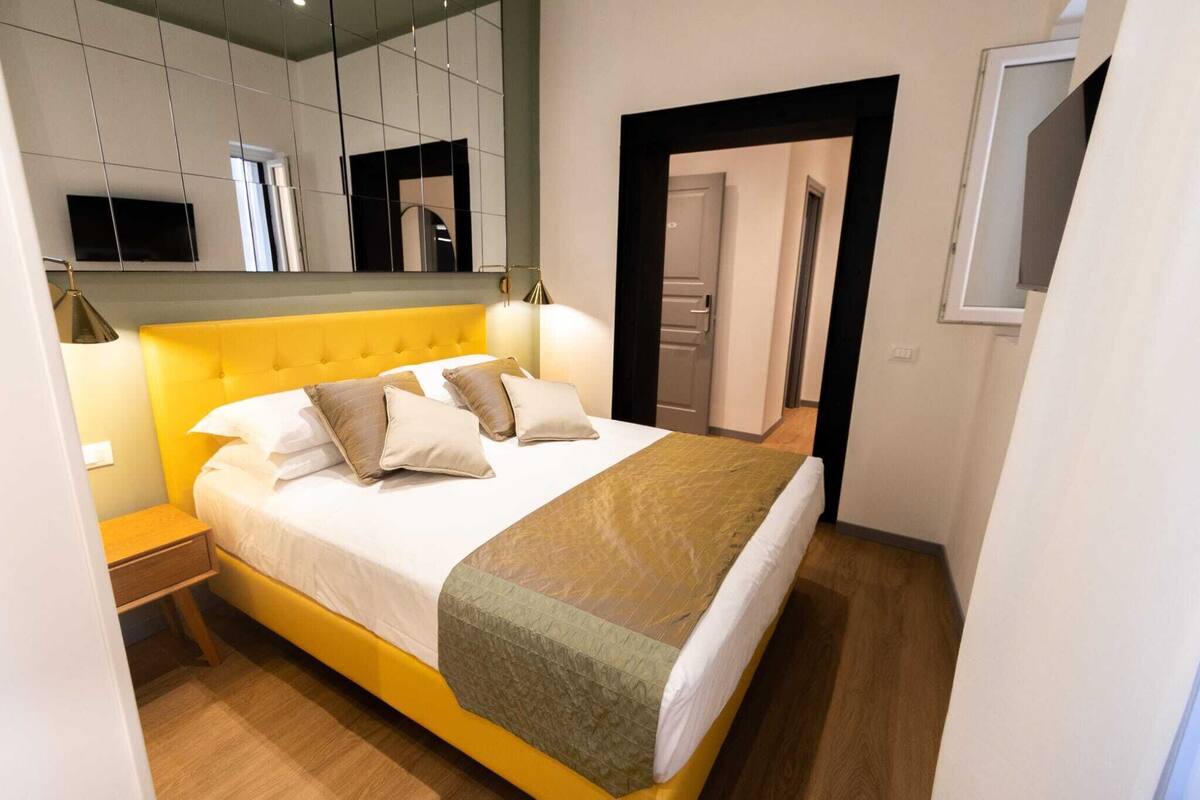 A modern bedroom with a yellow bed, white bedding, and a green throw blanket.