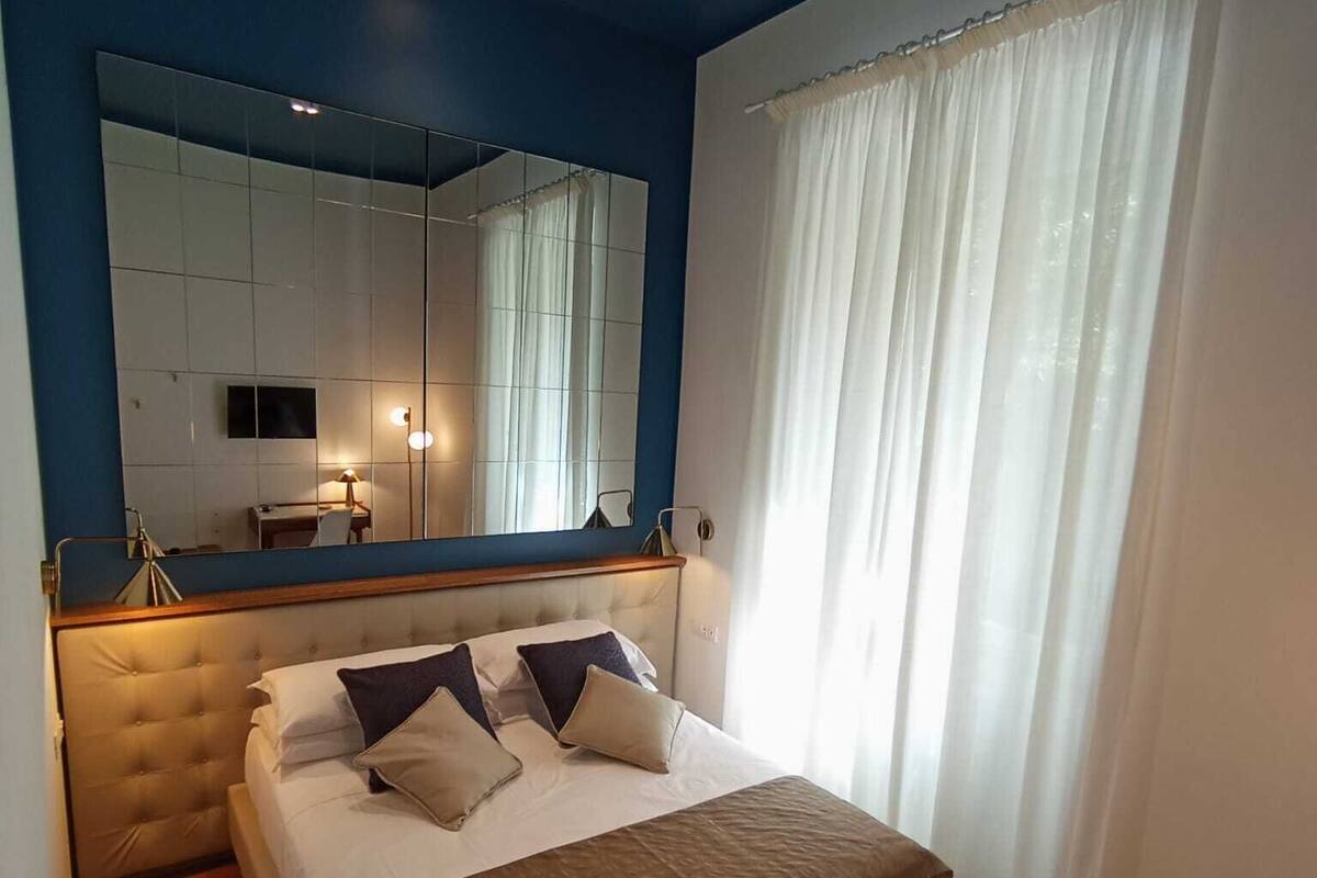 A modern bedroom with a large bed, a mirror, and a window with curtains.