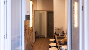 A narrow hallway with a wooden floor, a black mat at the entrance, and a table with chairs. - TREVI MONTI HOUSE  (Rome)