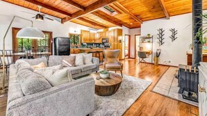 Amplia sala de estar con techo de madera, chimenea y cocina al fondo.