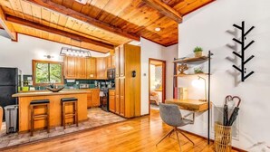 Una cocina moderna con armarios de madera, una isla central con taburetes y una zona de comedor con una silla y mesa.