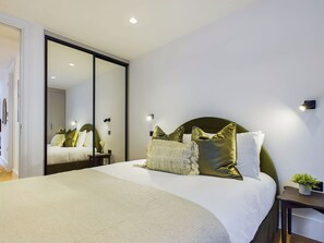 A modern bedroom with a large bed, a mirror, and a nightstand with a plant.