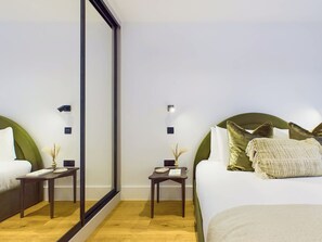 Ein Hotelzimmer mit einem großen Spiegel, zwei Nachttischen inklusive Lampen, einem Bett mit grünem Kopfteil und vielen Kissen sowie einem Holzboden.