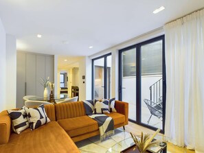 Ein modernes Wohnzimmer mit einem großen Ecksofa, einem Glastisch und Blick auf einen Balkon mit einer Treppe.
