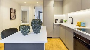A modern kitchen with a white countertop, two decorative vases, a coffee machine, and a sink with a black faucet. - Light-filled Maida Vale Mews Retreat (Greater London)