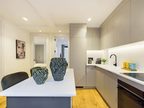 A modern kitchen with a white countertop, two decorative vases, a coffee machine, and a sink with a black faucet.