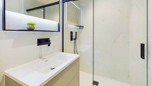 A modern bathroom with a white sink, a large mirror, and a glass-enclosed shower. - Light-filled Maida Vale Mews Retreat (Greater London)