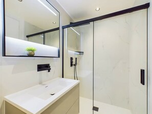Ein modernes Badezimmer mit einem weißen Waschbecken, einem großen Spiegel und einer Duschkabine.