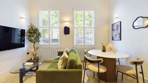 Un espace de vie compact comprenant un canapé vert, une table basse en verre, une table à manger ronde et un téléviseur fixé au mur.
