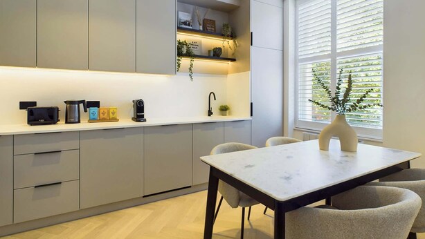 A modern kitchen with built-in cabinets, a dining table with chairs, and a window with blinds. - Beautiful, Premium Apartment in Maida Vale (Greater London)
