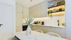 A modern kitchen with a marble countertop, a vase with greenery, and a shelf with coffee equipment. - Beautiful, Premium Apartment in Maida Vale (Greater London)
