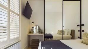 A modern bedroom with a bed, bedside table, mirror, and a wardrobe with a sliding door. - Beautiful, Premium Apartment in Maida Vale (Greater London)