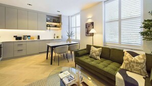 A modern living room with a green sofa, a glass coffee table, and a dining area with a white table and chairs. - Beautiful, Premium Apartment in Maida Vale (Greater London)