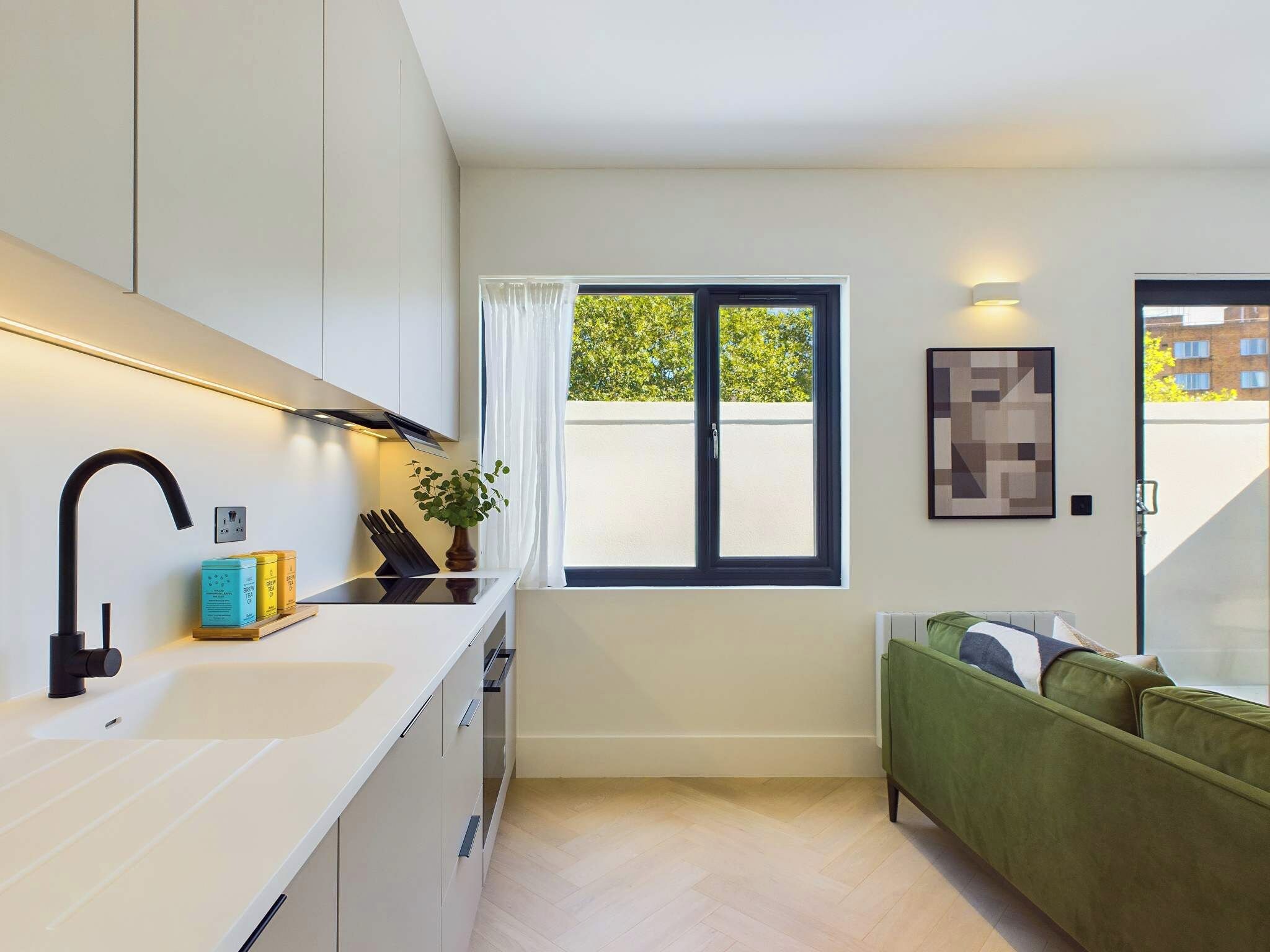 Eine moderne Küche mit weißer Arbeitsplatte, einem schwarzen Wasserhahn und einem Fenster mit Vorhängen.