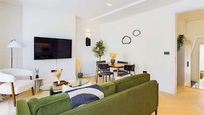 A modern living room with a green sofa, a glass coffee table, and a dining area with a small table and chairs.