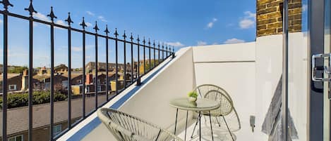 A balcony with two wicker chairs and a small table, overlooking a residential area.