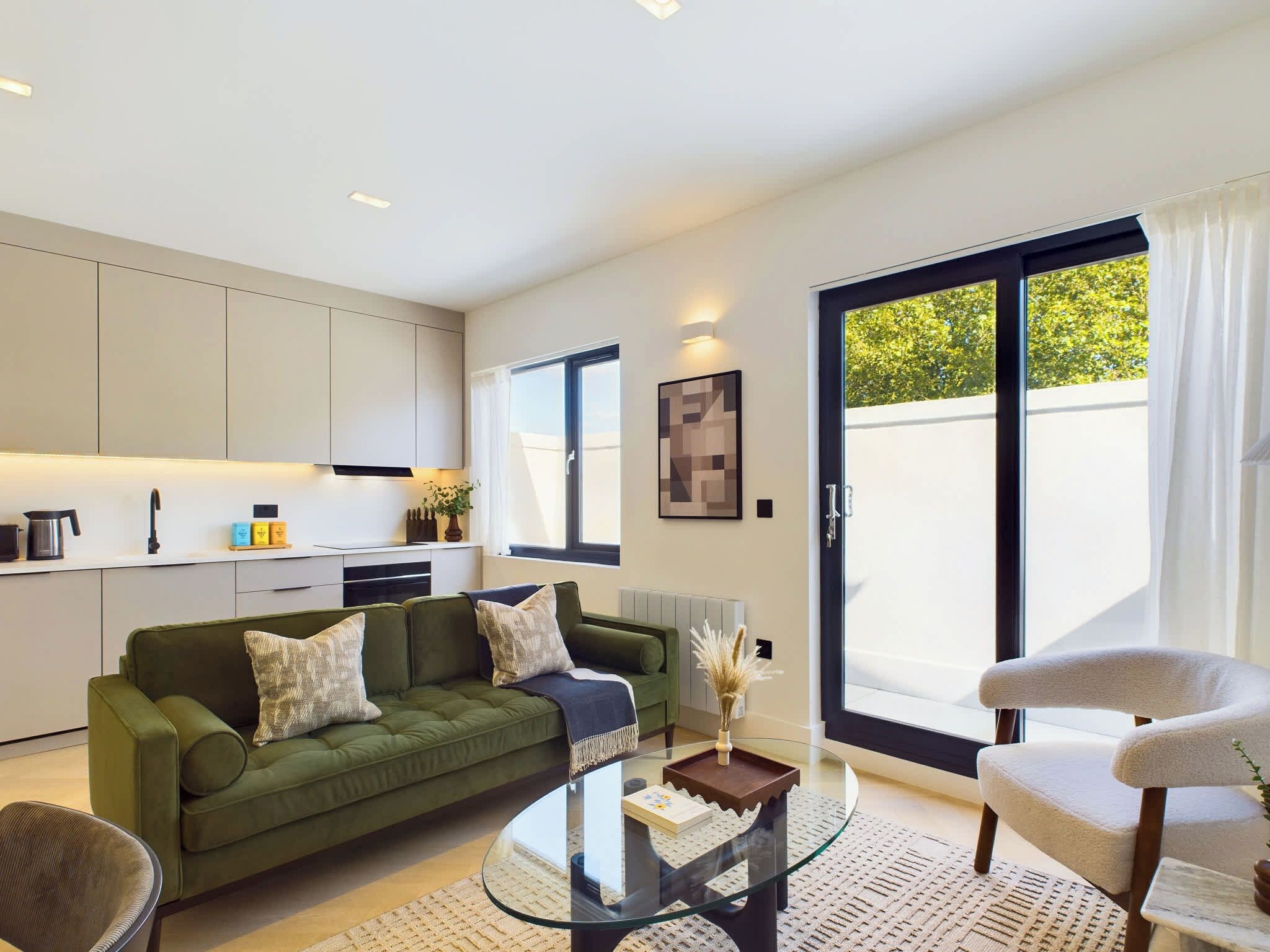 A modern living room with a green sofa, a glass coffee table, and a white armchair.