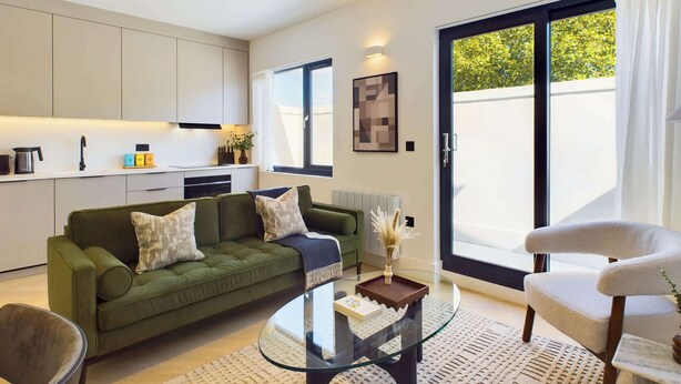 A modern living room with a green sofa, a glass coffee table, and a white armchair.