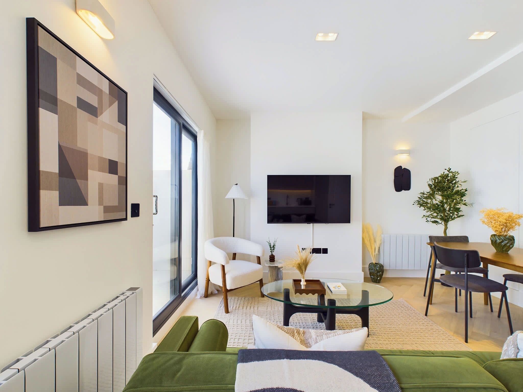 En moderne stue med et glasbord, grønne sofaer, et fladskærms-tv og et spiseområde med stole og et bord.