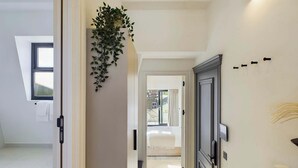 A hallway with a plant, a radiator, and a door leading to a room with a bed.