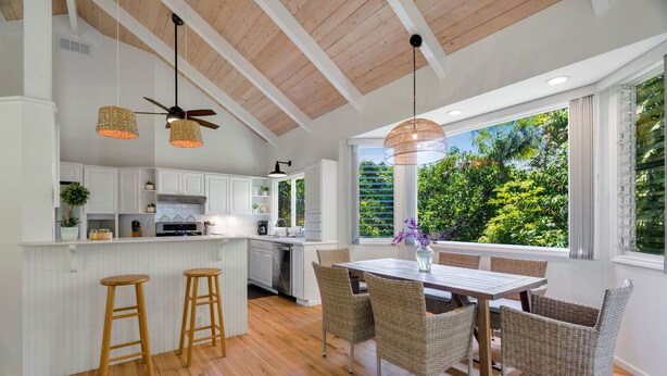 Une cuisine moderne avec des meubles blancs, un plancher en bois et un coin repas comprenant des chaises en osier et une table en bois.